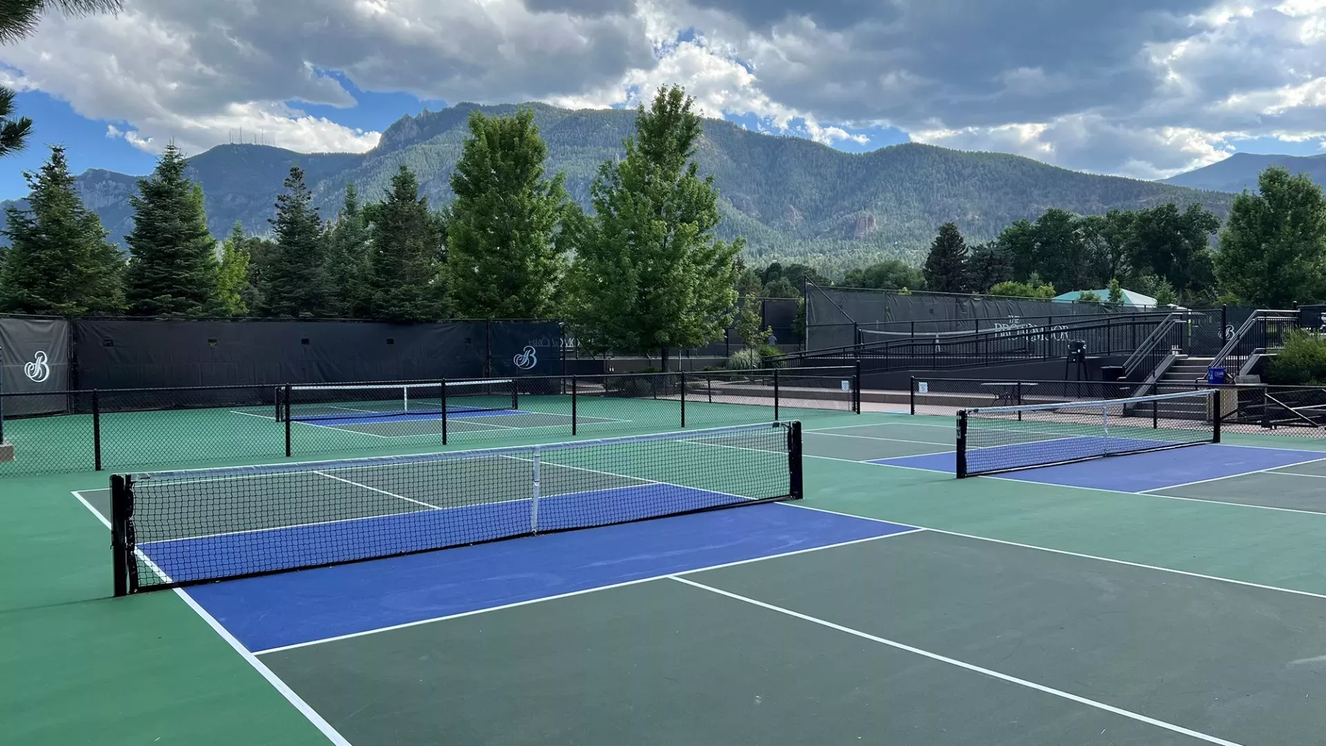 Four pickleball courts with pine trees and mountains in the background