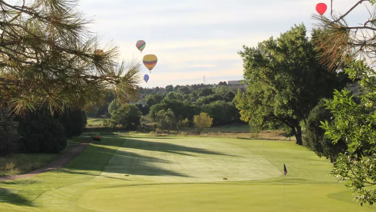 a golf course with hot air balloons flying in the distance